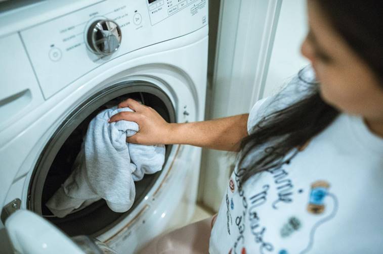 Vrouw stopt kleding met een vlek in de wasmachine voor reiniging