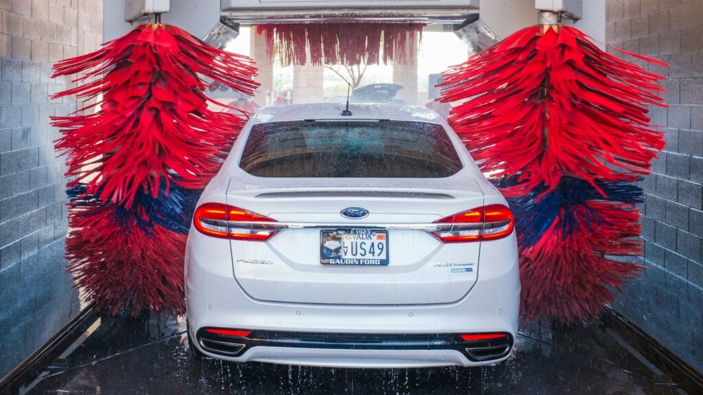 Witte auto wordt gewassen in een moderne wasstraat met roterende rode borstels – auto wassen