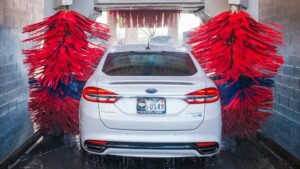Witte auto wordt gewassen in een moderne wasstraat met roterende rode borstels – auto wassen
