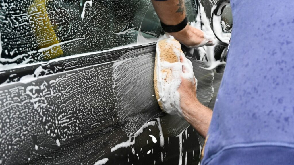 Handmatig carwrap onderhoud met spons en sop op zijde van een auto