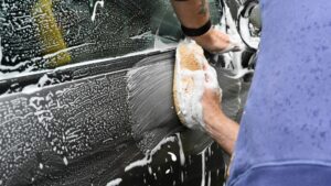 Handmatig carwrap onderhoud met spons en sop op zijde van een auto