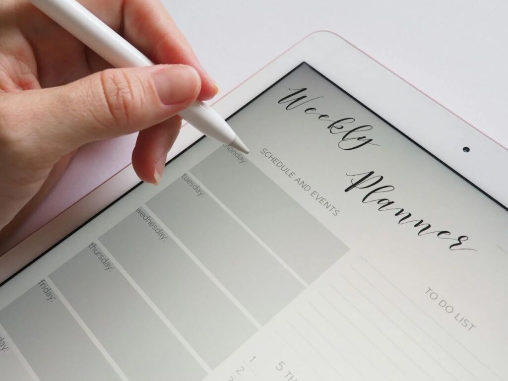 Hand gebruikt stylus om te schrijven in een digitale weekplanner met dagen van de week