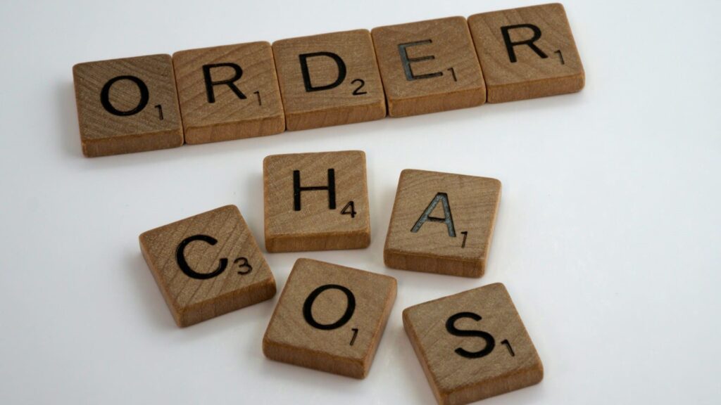 Houten letters spellen het woord “ORDER” terwijl het woord “CHAOS” door elkaar ligt, symbool voor orde en netheid.